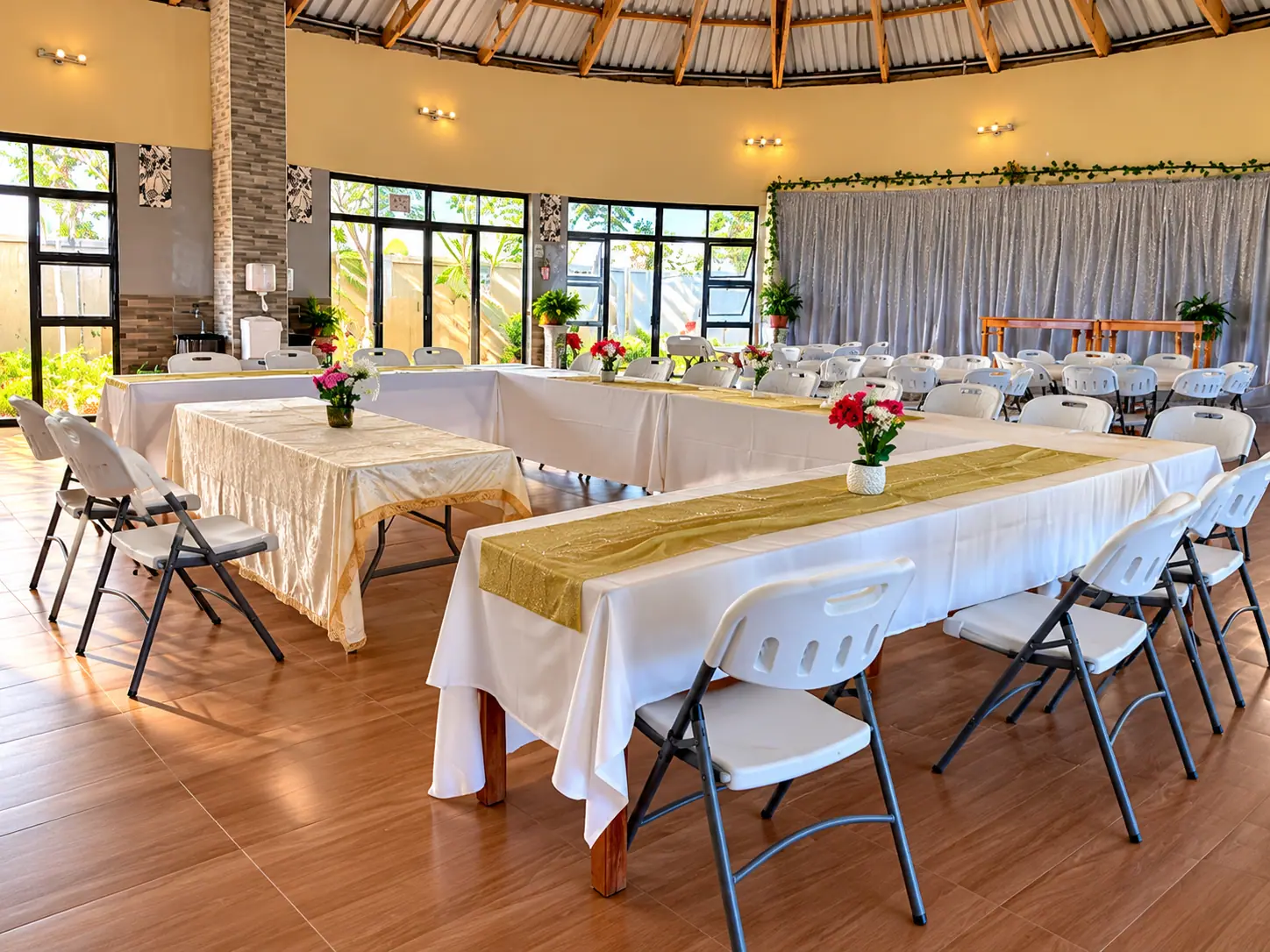 Tables arranged in a U-shape with gold runners and fresh flowers, with a draped backdrop