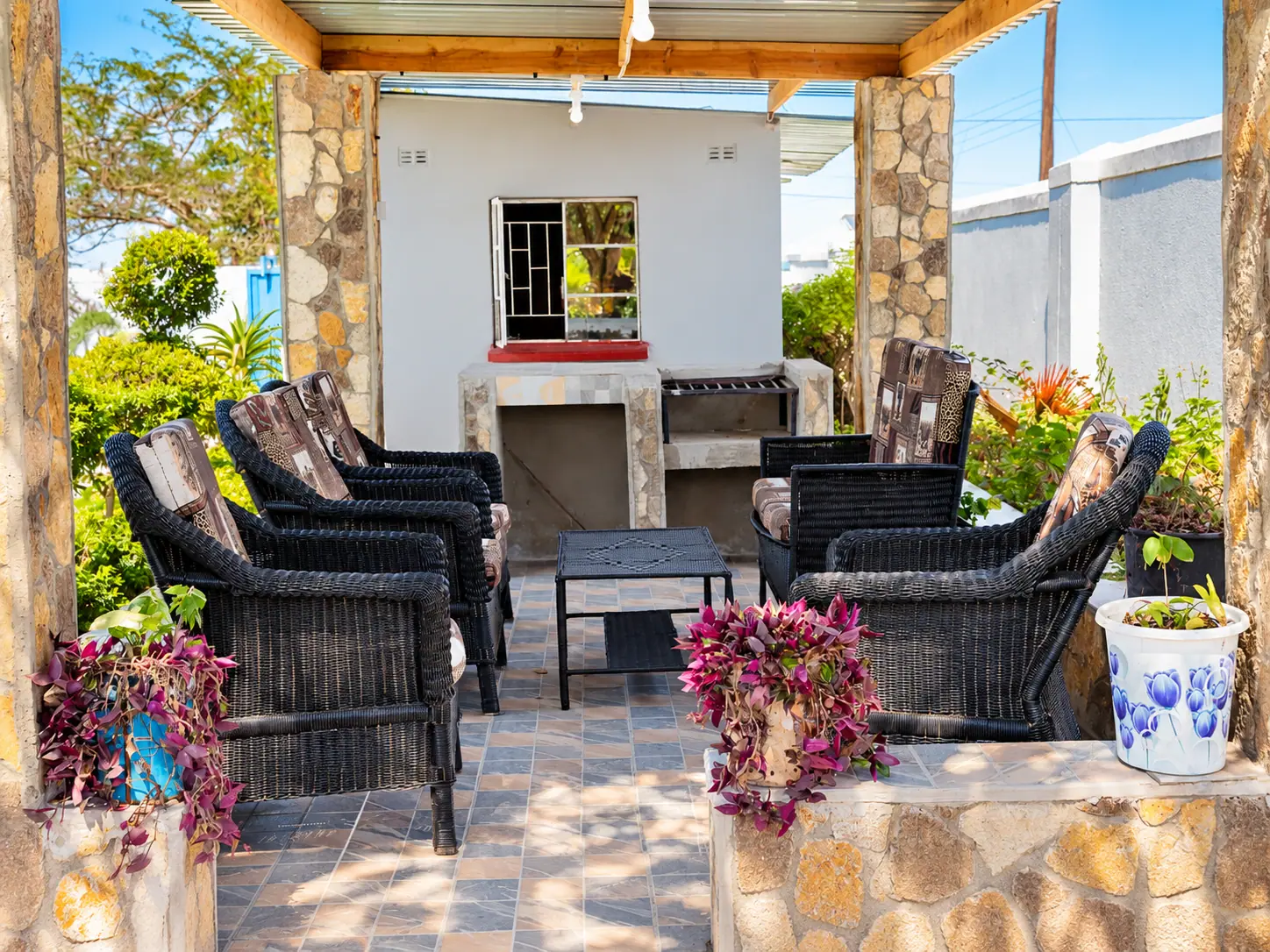 Wicker armchairs around a low table under the pergola, with the built braai stand behind