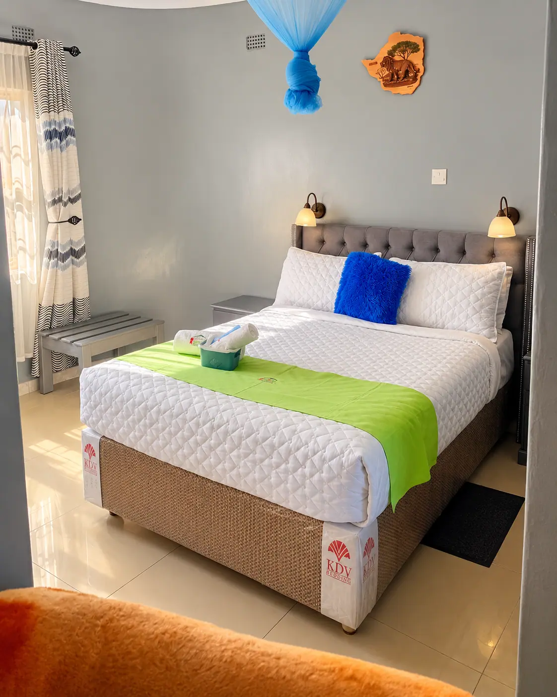 A double bed with a blue cushion, green runner and a knotted blue mosquito net