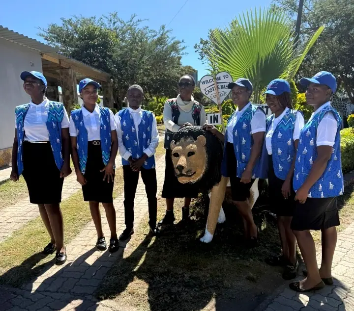 The Castle Base Lodge team in blue patterned waistcoats and caps beside the lion statue at the entrance